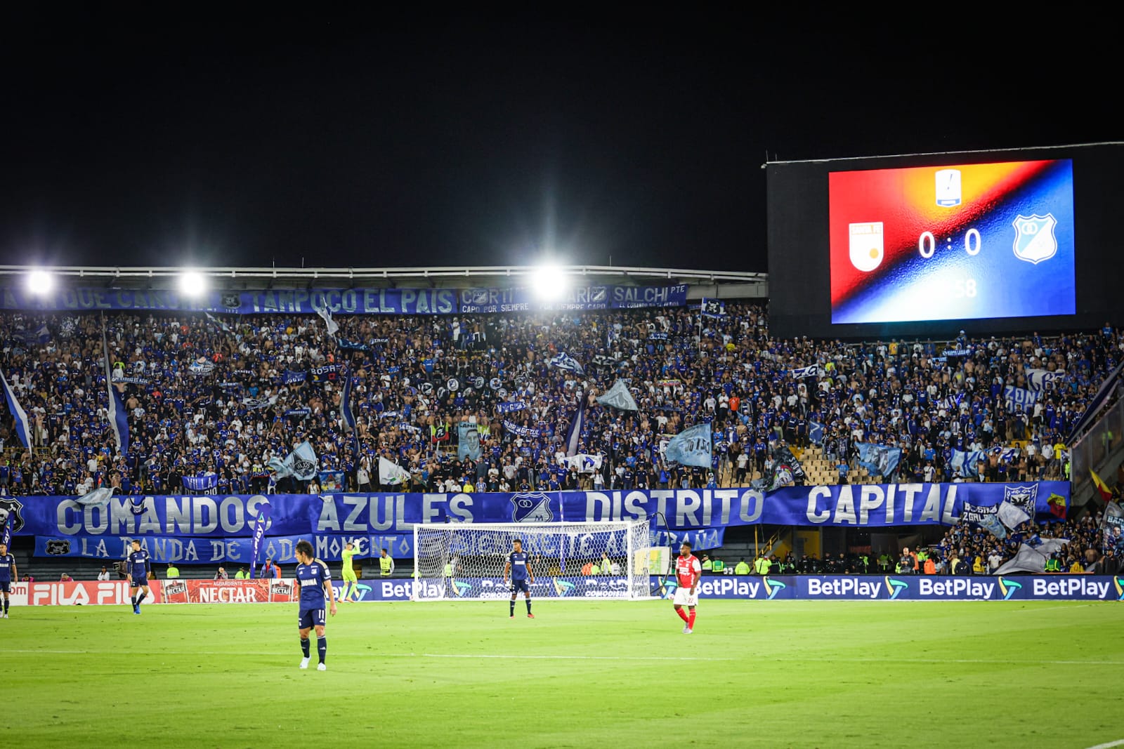 Foto panoramica de una parte del Campín donde se ve el arco y de fondo la hinchada de Millonarios alentando a su equipo