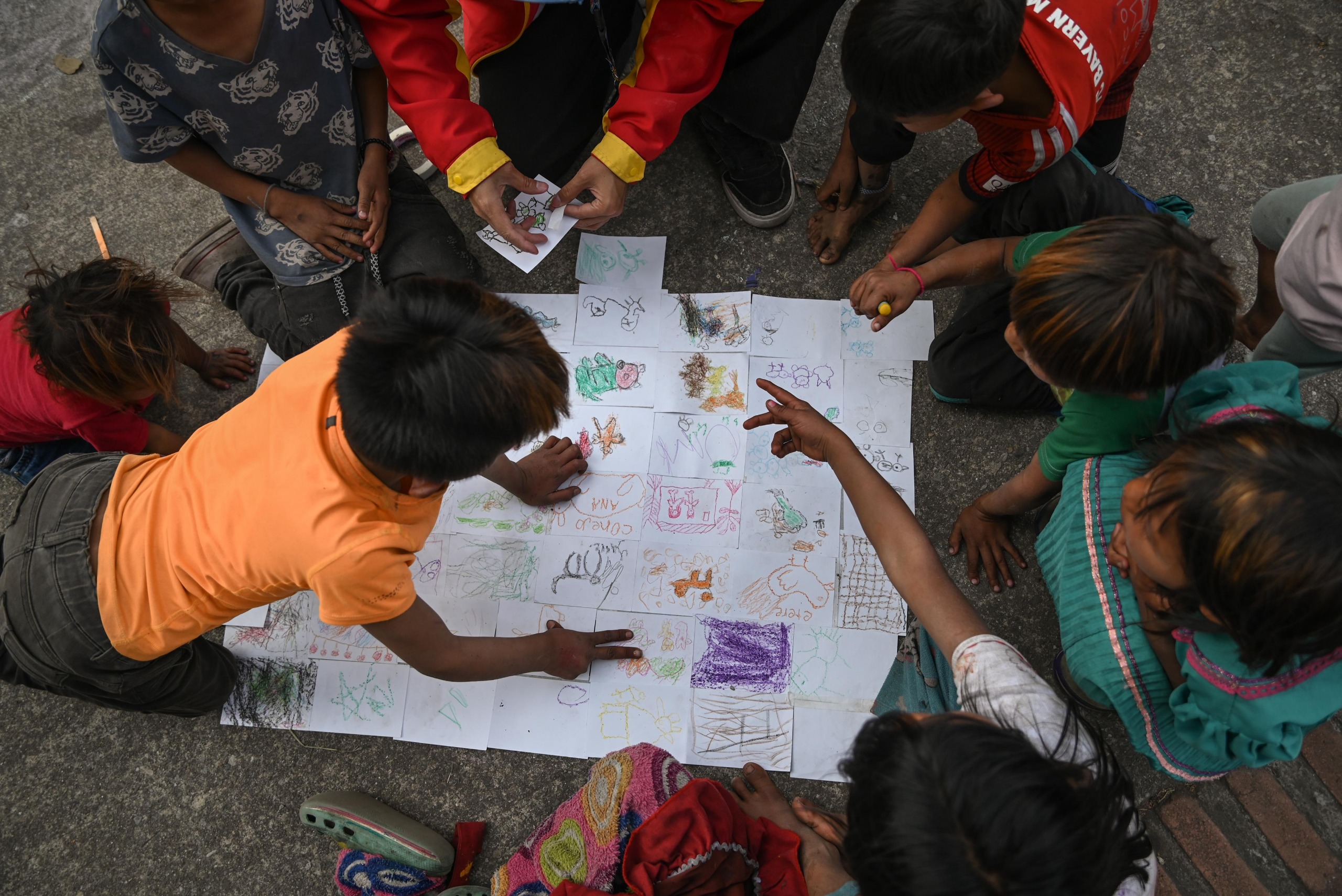 Foto cenital donde se aprecian niñas y niños Embera realizando diferente dibujos y organizandolos sobre el piso