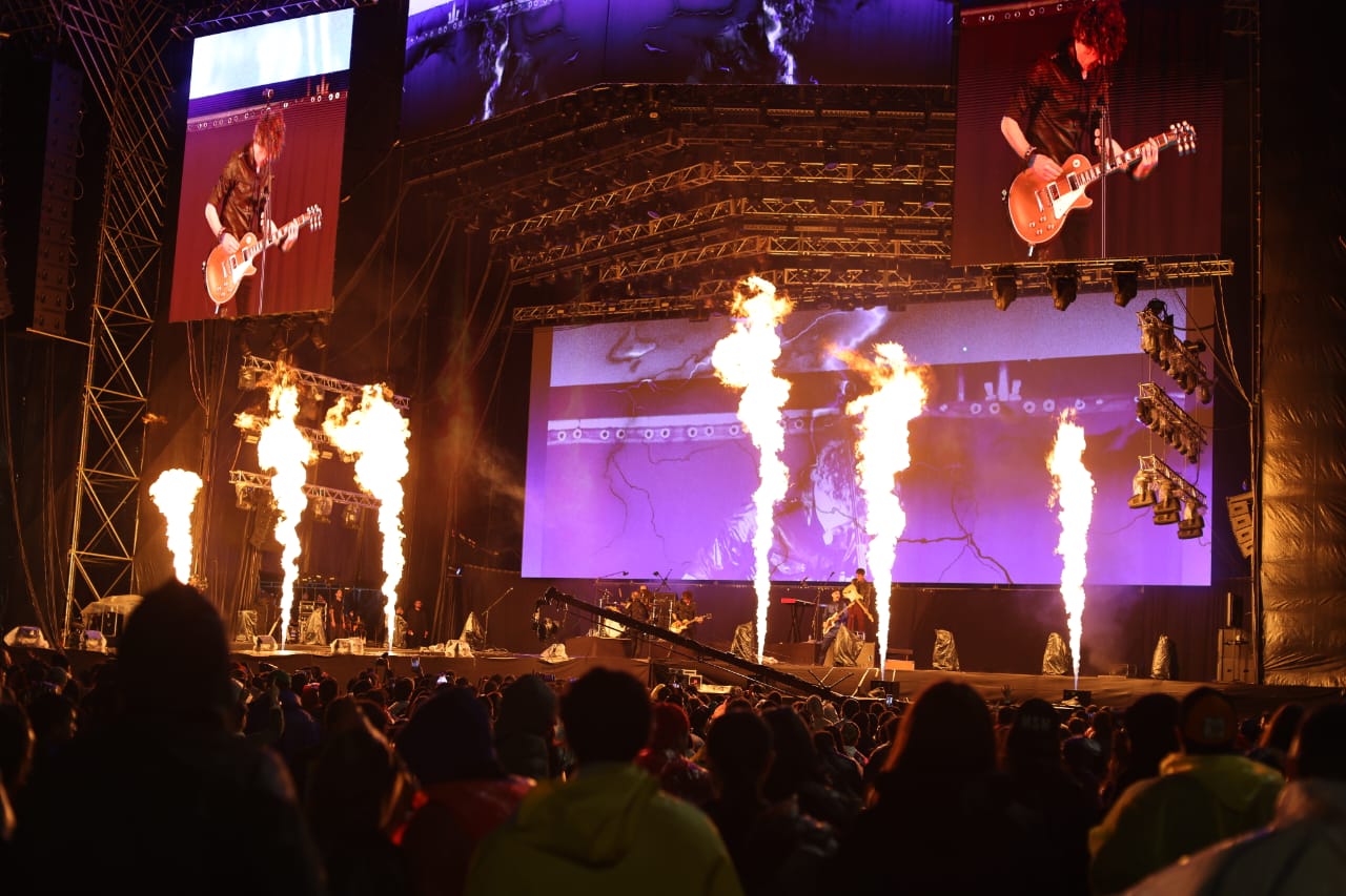 Foto de un escenario en la noche con fuego saliendo previo a la presentacion de una banda musical