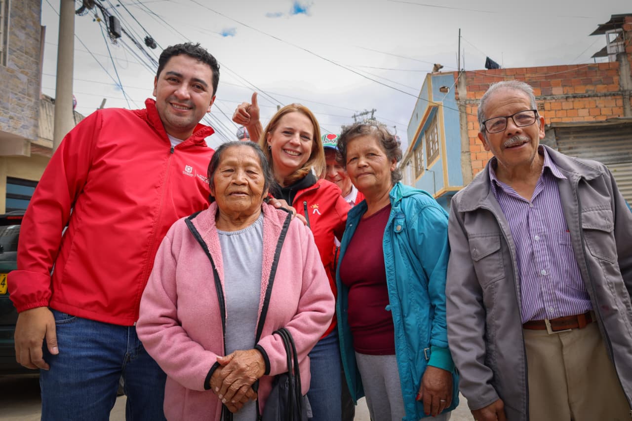 Foto de dos funcionarios de la localidad y la SDG acompñando la felicidad de cuatro personas mayores vecinos del barrio