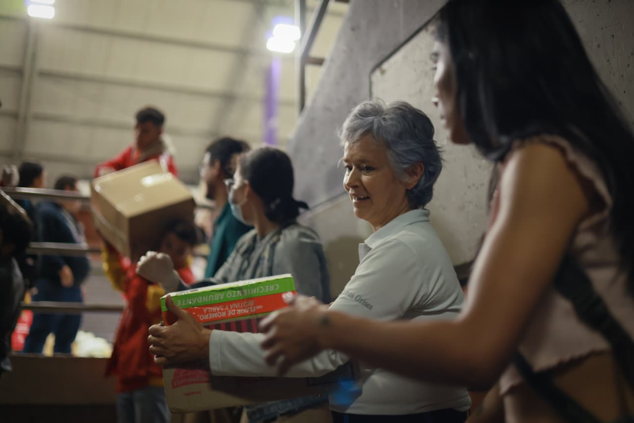 Foto de una cadena humana pasando donaciones, se enfoca en una mujer de la tercera edad