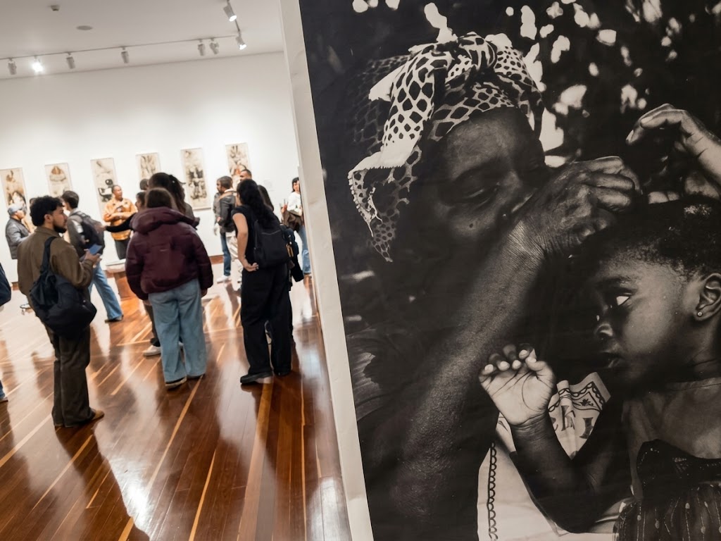 Foto de una fotografia de la exposicion y al fondo se ve el publico recorriendo el espacio expositivo