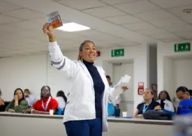 Fotografía de una mujer con chaqueta blanca dirigiendose a la audiencia
