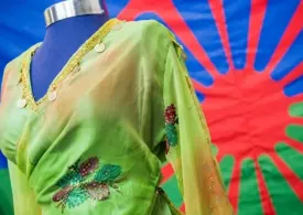 Foto de un vestido de mujer caracteristico del pueblo Rrom y de fondo la bandera del pueblo Rrom