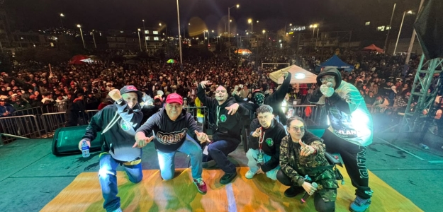 Artistas posan sobre el escenario frente a una multitud durante un festival de hip hop nocturno, en un ambiente lleno de energía, música y cultura urbana.