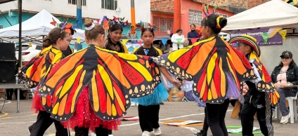 Grupo de niñas y jóvenes participa en una presentación cultural con coloridas alas de mariposa en un espacio comunitario al aire libre.