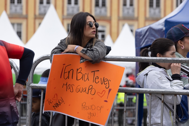 Foto de una joven con una cartelera animando a los ciclistas