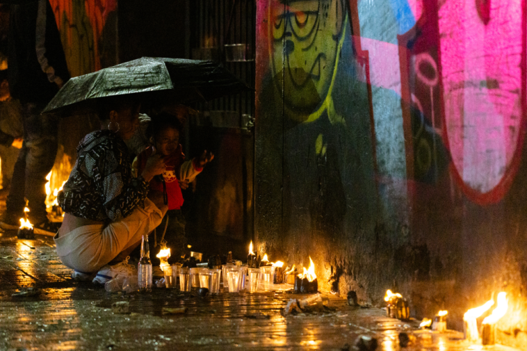 Foto de una joven mujer con su hija pequeña bajo la lluvia viendo las velas de la calle