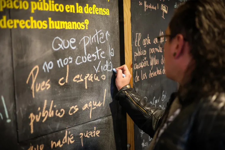 Foto de una mujer escribiendo un mensaje sobre un talbero de fondo negro.