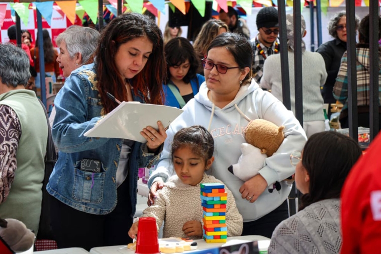 Foto de madre e hija pequeña en la feria hablando con una joven de cabello ondulado