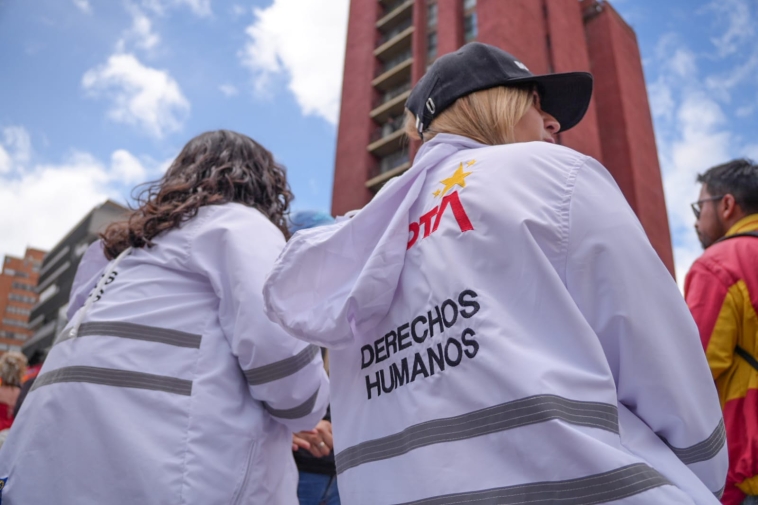 Foto de dos funcionarias de la SDG de chaqueta blanca de espaldas observando la marcha