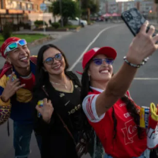 Fotografía de tres hinchas con sus camisetas de futbol felices tomandose una selfie en el barrio