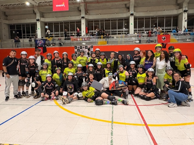 Participantes de un torneo de roller derby posan en grupo dentro de un escenario deportivo, con uniformes, cascos y patines, en un ambiente de celebración, integración y compañerismo.
