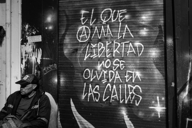 Grafiti en una fachada de local comercial y un señor sentado al lado