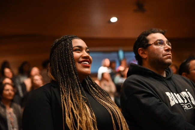 Mujer joven sonriendo, a su lado jóven prestando atención a la charla