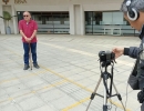 Foto de dos personas, una con una cámara grabando a un hombre que se encuentra de pie mirando a la cámara