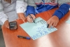 Foto donde se aprecian las manos de un menor de edad escribiendo nñumeros sobre una cartulina y a su lado se aprecian las manos de una persona adulta.